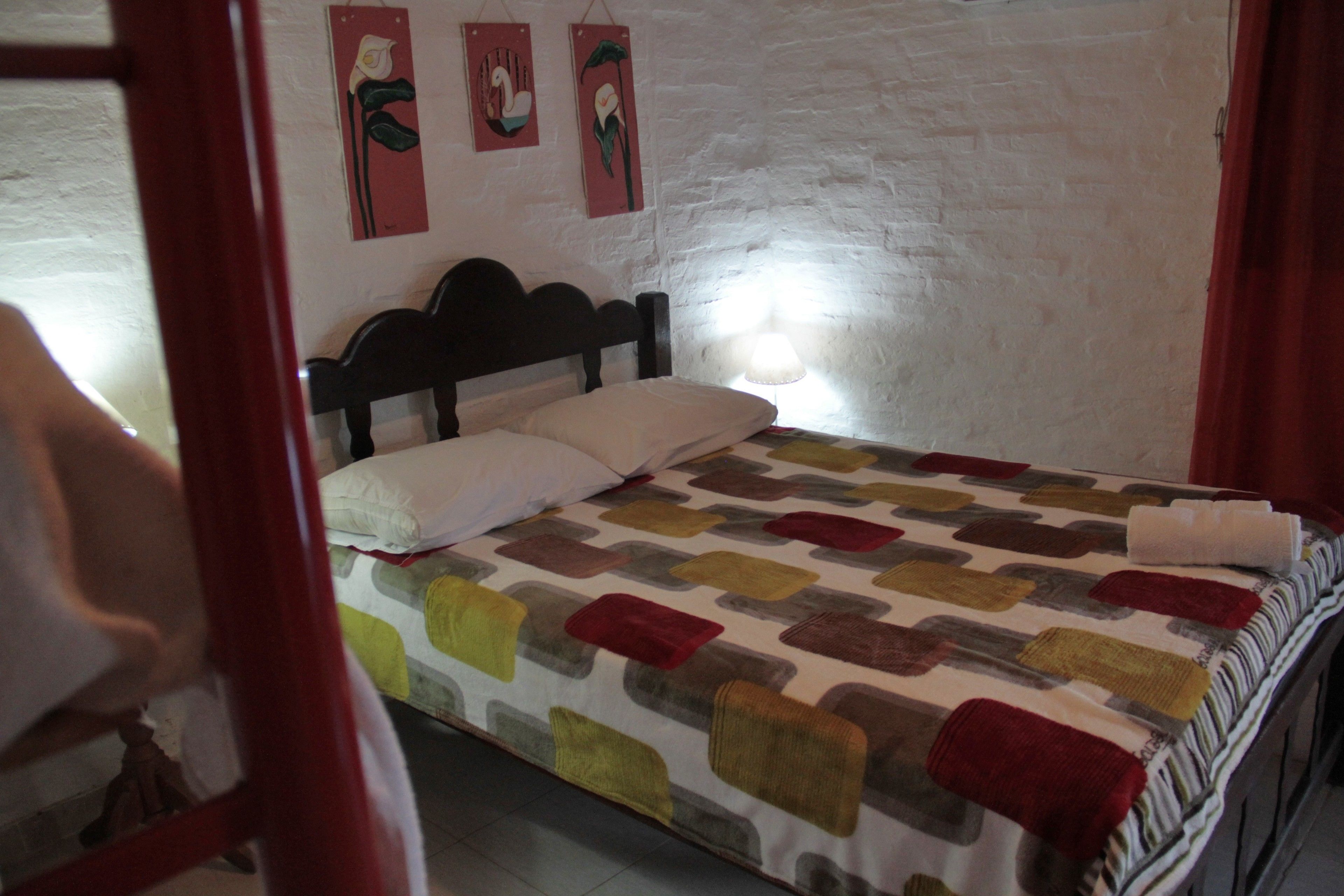 A bed with a patterned bedspread, a wooden headboard, and two wall-mounted artworks.