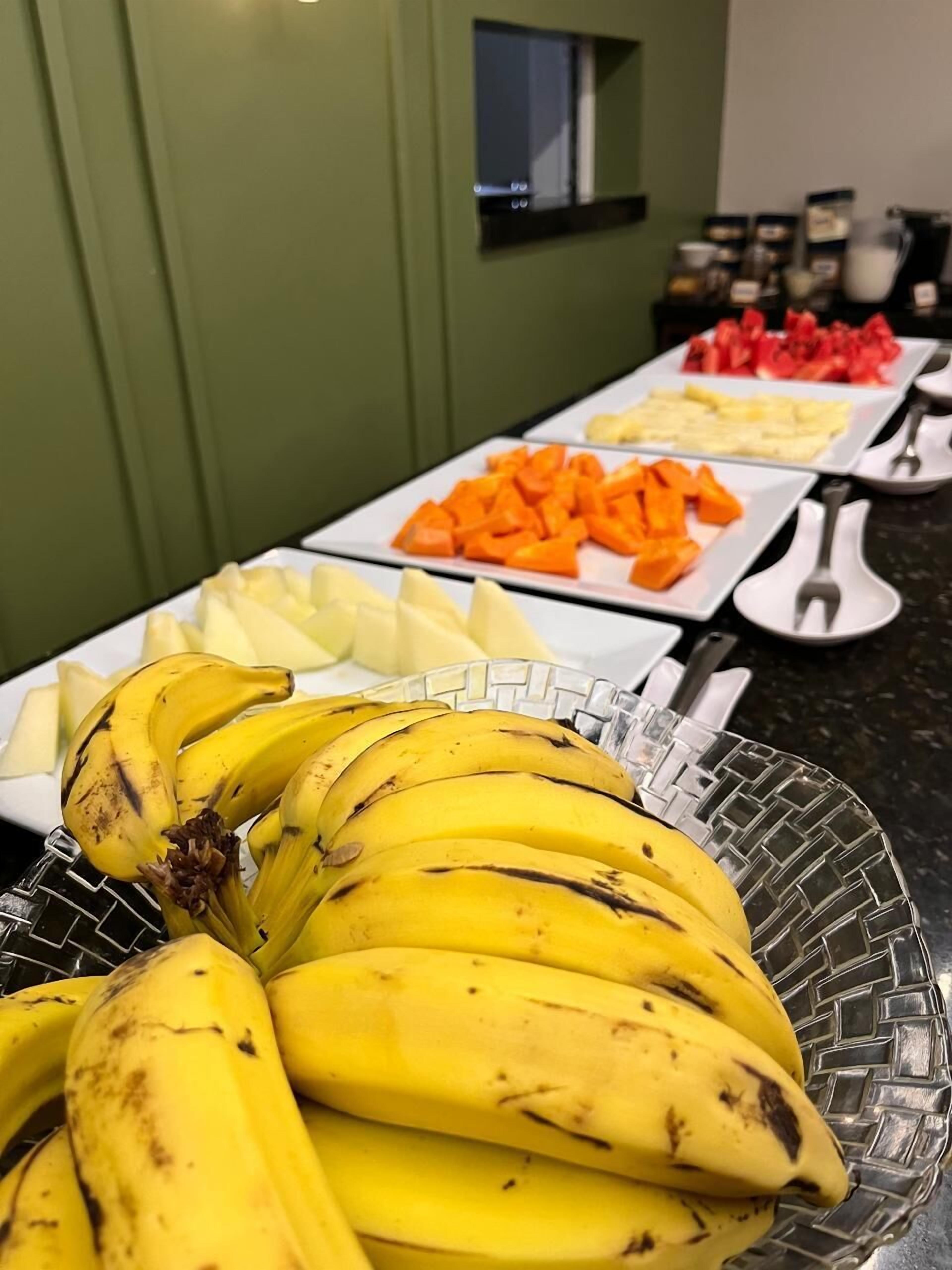 A buffet with various fruits and a glass bowl of bananas.