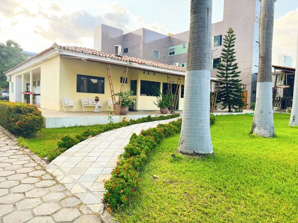 Un hotel con techo de tejas, un patio cubierto con sillas y un césped bien cuidado.