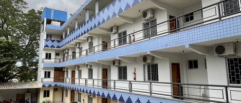 A multi-story building with balconies, air conditioning units, and a parking area with a car.