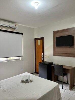 Una habitación de hotel con cama, escritorio, silla, televisor y aire acondicionado.