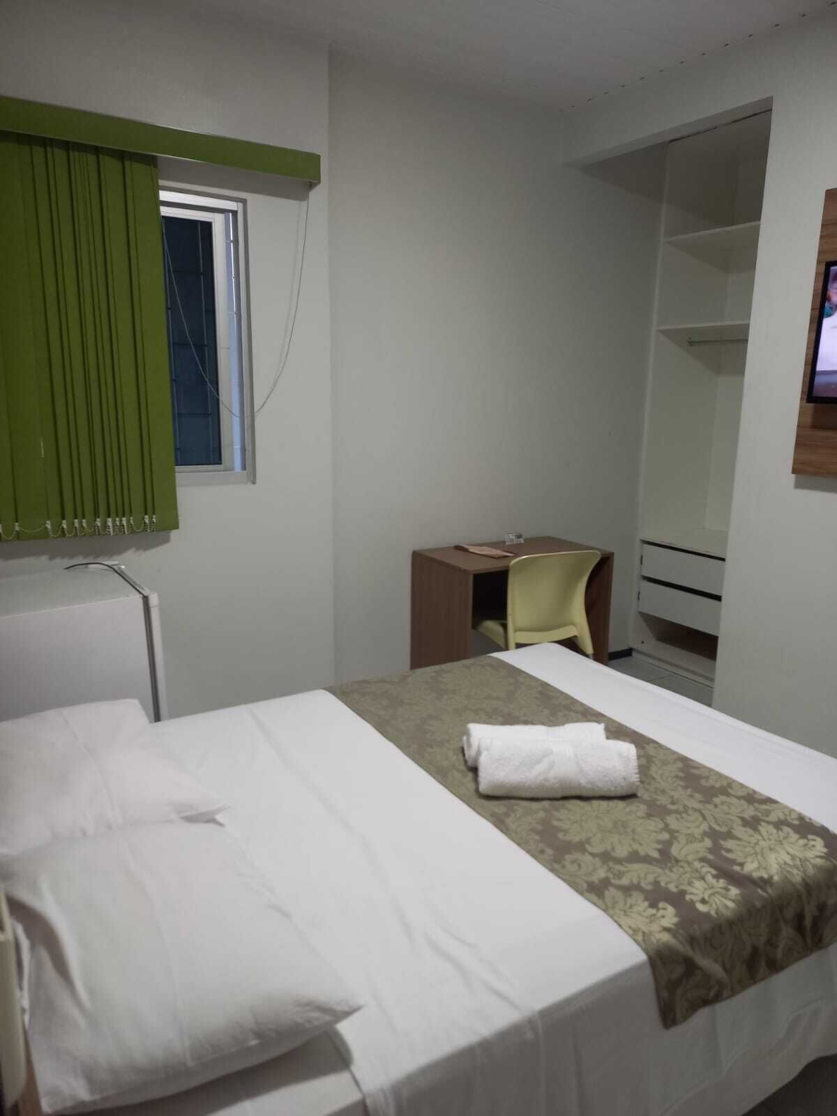 A hotel room with a bed, a desk, a chair, a wardrobe, and a television.