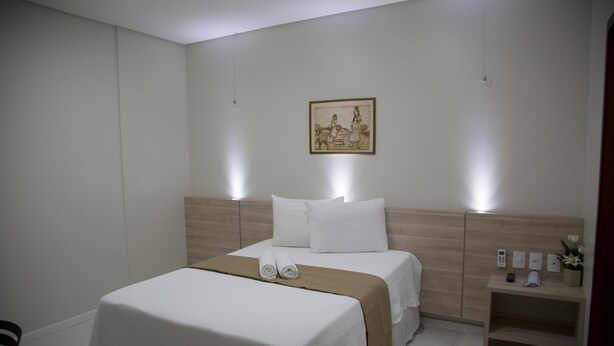 A hotel room with a bed, bedside tables, a nightstand, and a wall-mounted picture. - Hotel Padre Cícero (Juazeiro do Norte)