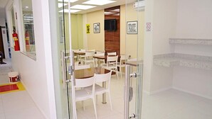 A modern dining area with glass partitions, white chairs, and a wooden table. - Hotel Padre Cícero (Juazeiro do Norte)
