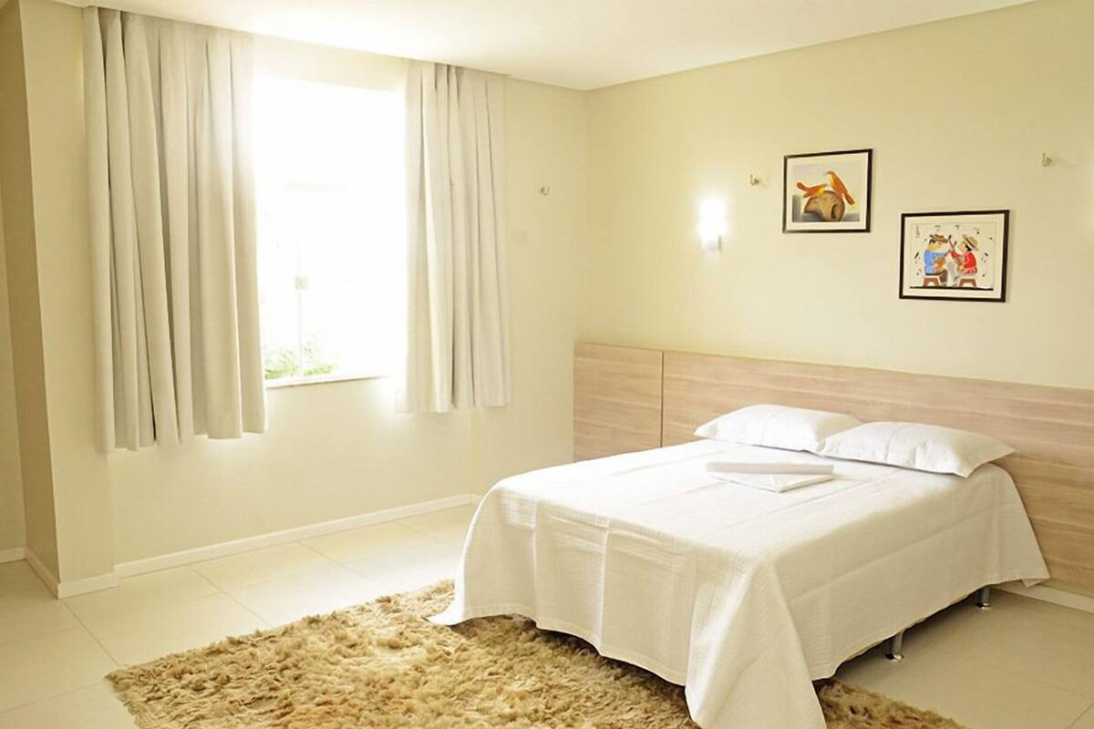 Une chambre à coucher avec un lit, des rideaux et deux tableaux encadrés accrochés au mur.