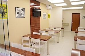 Un comedor con mesas y sillas, un televisor montado en la pared y obras de arte enmarcadas en las paredes.