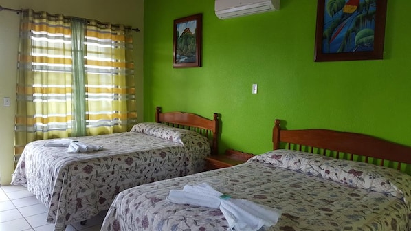 A room with two beds, green walls, a painting, and an air conditioner. - Anchorage Beach Resort (Caye Caulker)