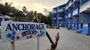 A sign for Anchorage Resort with a sandy beach and blue buildings in the background. - Anchorage Beach Resort (Caye Caulker)