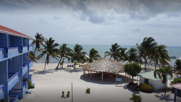 Una playa con palmeras, una estructura de techo de paja y un edificio azul con balcones decorados.