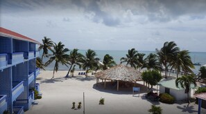 Una playa con palmeras, una estructura de techo de paja y un edificio azul con balcones decorados.