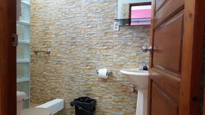 Un baño con pared de piedra, un inodoro, un lavamanos y un cubo de basura.