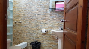 A bathroom with a stone wall, a toilet, a sink, and a trash bin. - Anchorage Beach Resort (Caye Caulker)