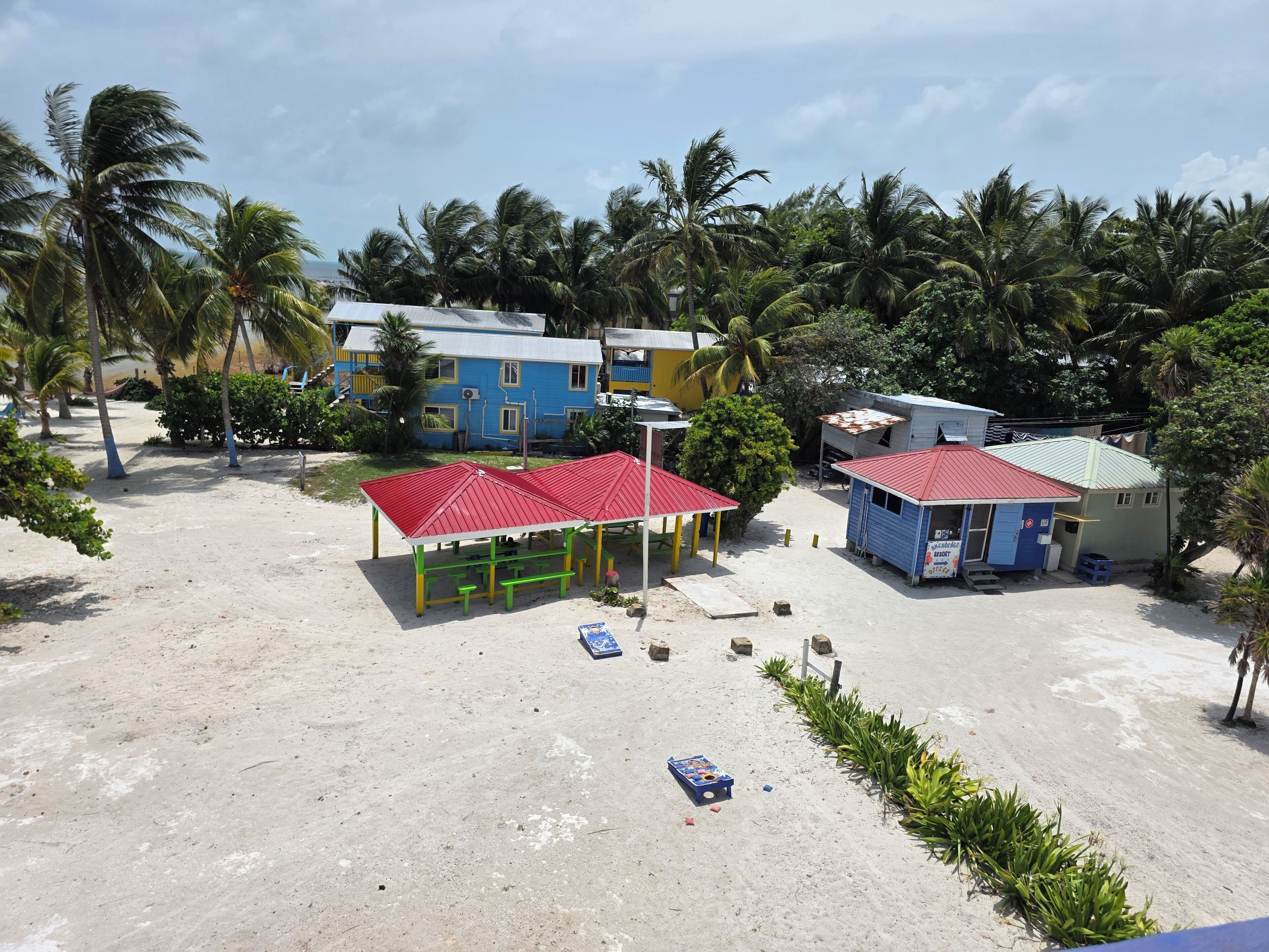 Una propiedad frente a la playa con un pabellón de techo rojo, una pequeña oficina azul y un edificio amarillo.
