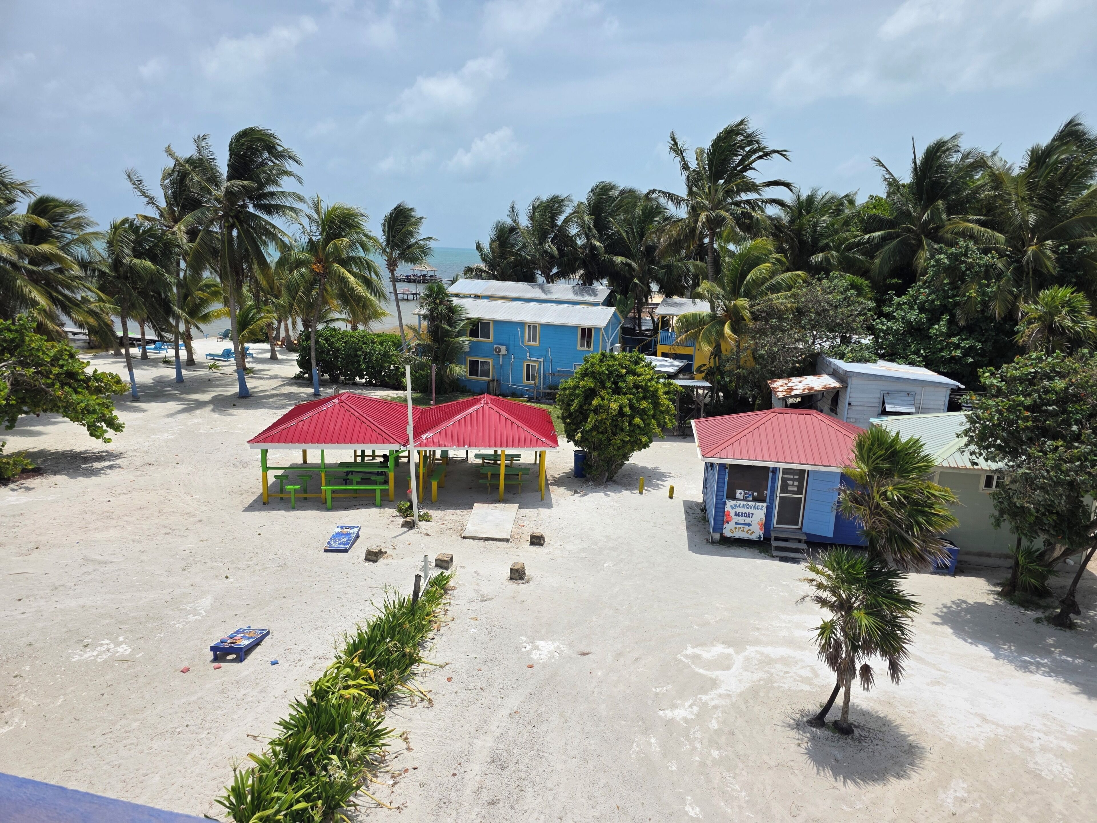 A beachside resort with multiple red-roofed structures, palm trees, and a sandy beach.