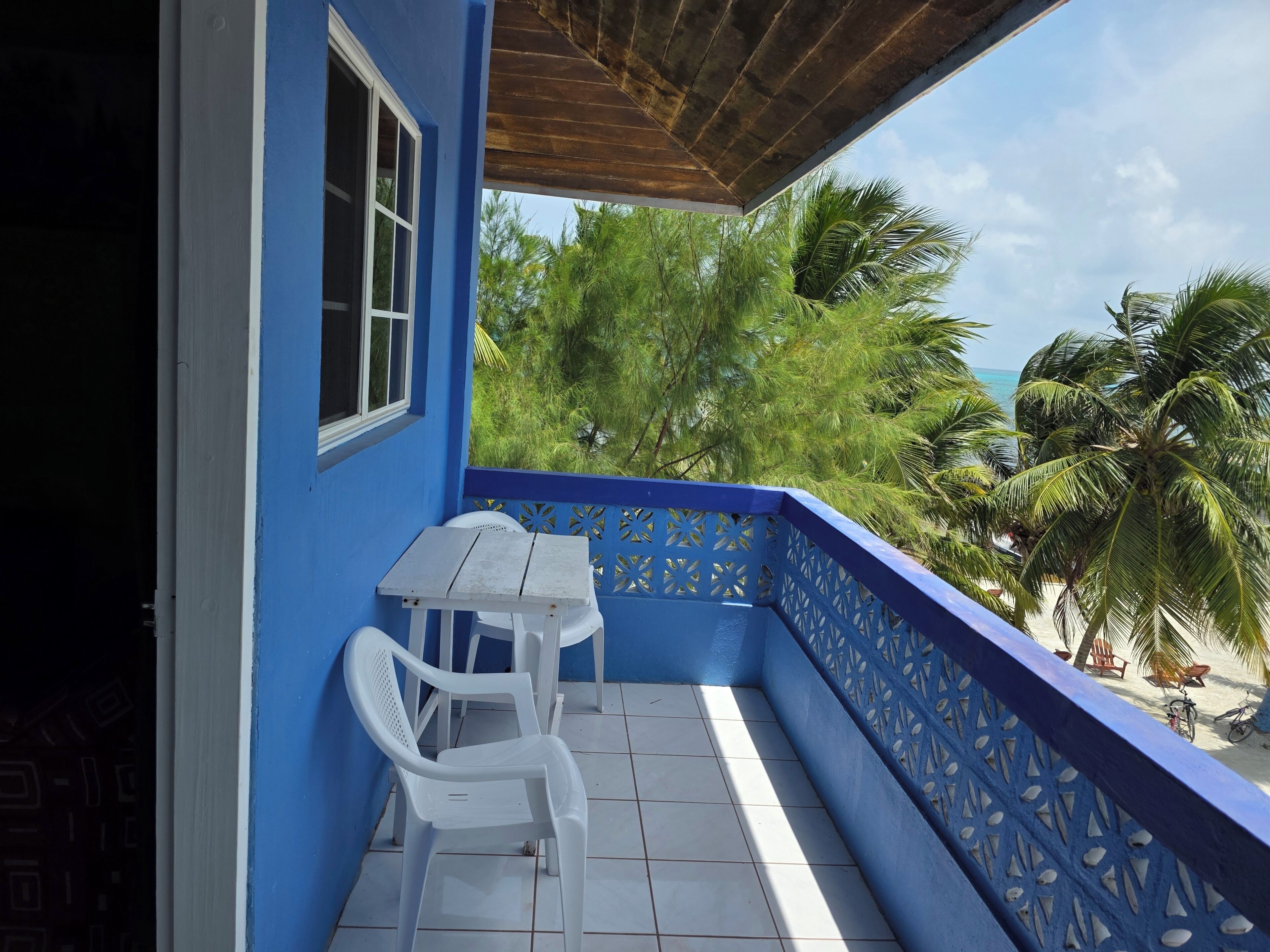 A balcony with a blue railing, a white table, and two white chairs.