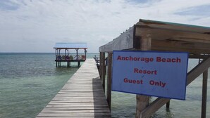 Un muelle de madera que conduce a una estructura sobre el agua, con un letrero que indica 'Anchorage Beach Resort Guest Only'.