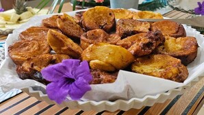 A tray of fried plantains on a table with a decorative purple flower.