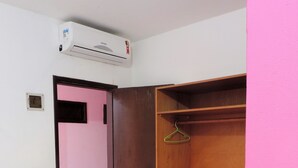 A room with a wooden wardrobe, a small stool, and an air conditioning unit on the wall.
