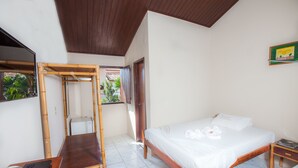 A hotel room with a bed, a desk with a laptop, a chair, and a window with a view of greenery.