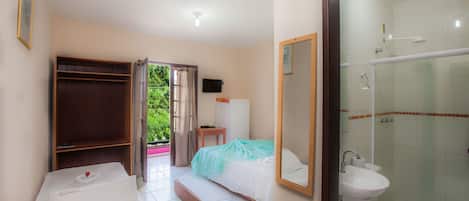 A hotel room with a bed, a bathroom with a sink and toilet, and a view of greenery outside.