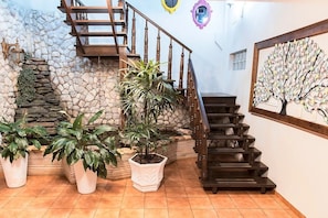 Una escalera con pared de piedra y barandillas de madera, rodeada de plantas en macetas.