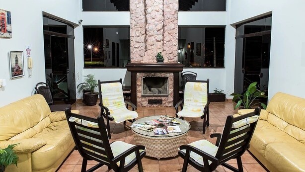 A modern living room with a stone fireplace, yellow leather sofas, and a round coffee table. - Pousada Villa Guimarães (Chapada dos Guimarães)