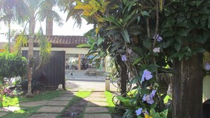 A pathway leading to a building with a tiled roof, surrounded by lush greenery and flowering plants. - Pousada Villa Guimarães (Chapada dos Guimarães)