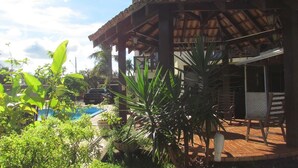 A pool area with a wooden deck, surrounded by lush greenery and a thatched-roof structure. - Pousada Villa Guimarães (Chapada dos Guimarães)