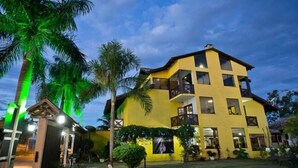 A multi-story yellow building with balconies, surrounded by palm trees and a well-maintained lawn. - Pousada Villa Guimarães (Chapada dos Guimarães)