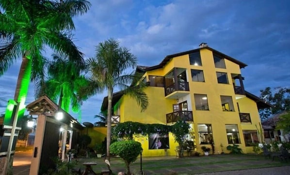 Un edificio amarillo de varios pisos con balcones, rodeado de palmeras y un césped cuidado.