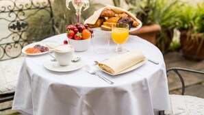 A round table with a white tablecloth, a plate of croissants, a bowl of fruit, a cup of coffee, a glass of orange juice, and a folded napkin. - Hotel Santo Stefano (Venice)