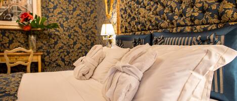 A neatly made bed with two towels, a headboard with a floral pattern, and a framed picture on the wall.
