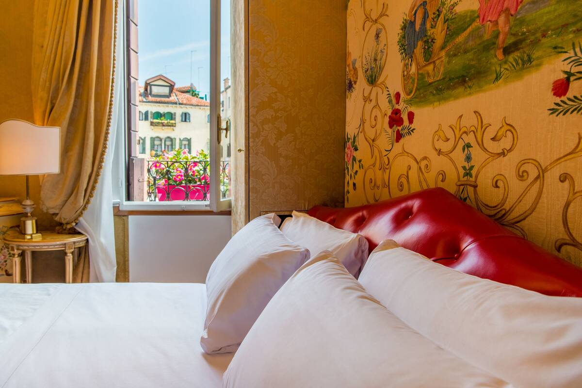 A hotel room with a bed, a window with a view of buildings, and a lamp on a side table.