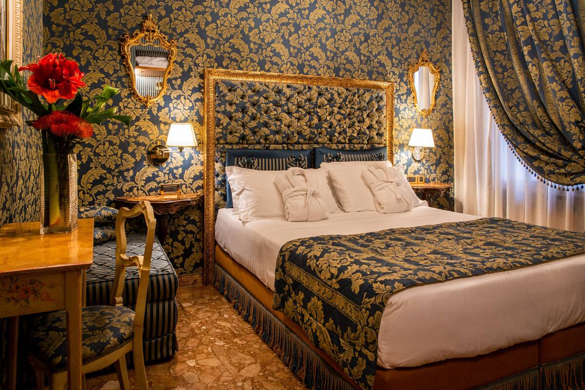 A bedroom with a large bed, two bedside tables with lamps, a mirror, and a floral-patterned wall.