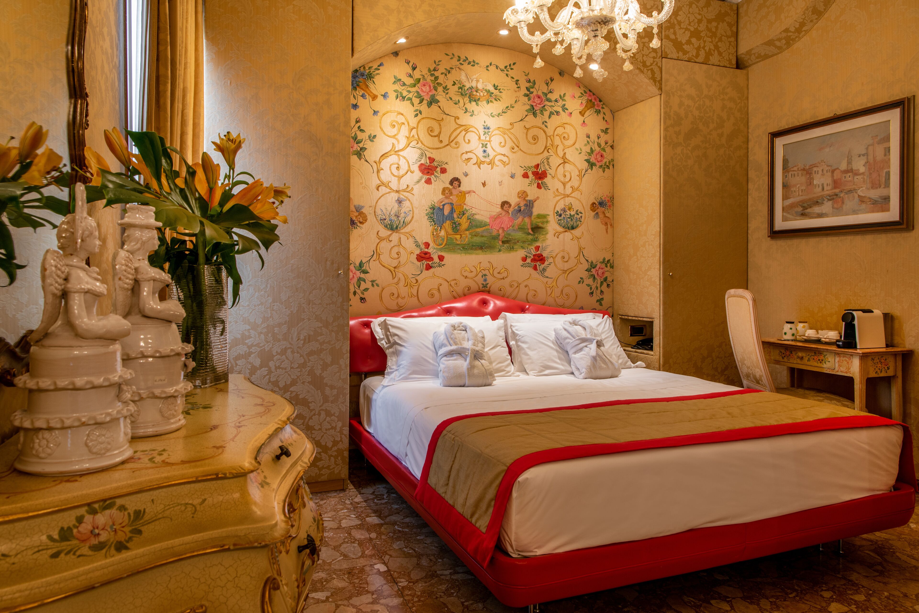 Ein Hotelzimmer mit einem großen Bett, einem Schminktisch mit Dekorationen, einer Kristallleuchtre und einem blumigen Wanddesign.