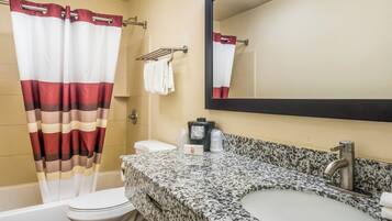 A bathroom with a striped shower curtain, a toilet, a sink with a granite countertop, a mirror, and a towel rack.