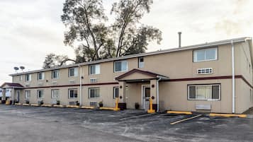 A motel with a row of rooms, a parking lot, and trees in the background.