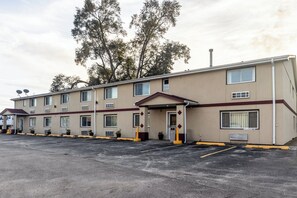 A motel with a row of rooms, a parking lot, and trees in the background. - Red Roof Inn Chicago - Alsip (Alsip)