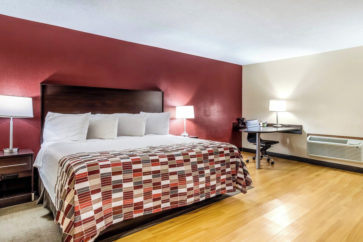 A hotel room with a bed, two bedside lamps, a desk with a chair, and a radiator.