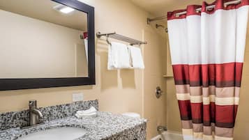 Un baño con lavamanos de encimera de granito, un espejo, un perchero con dos toallas blancas, una cortina de ducha y una bañera.