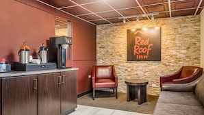 A Red Roof Inn lounge with a stone wall, leather seating, a coffee machine, and a small table. - Red Roof Inn Chicago - Alsip (Alsip)
