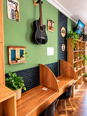 A room with a wooden desk, a guitar, and a TV on the wall. - Estacion Mendoza Hostel (Mendoza)