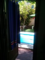 Vista de una piscina con terraza de madera y un árbol al fondo.