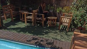 A swimming pool with wooden deck chairs and tables, surrounded by potted plants. - Estacion Mendoza Hostel (Mendoza)