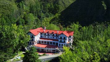 A large, multi-story building with a red roof, surrounded by dense forest and hills.