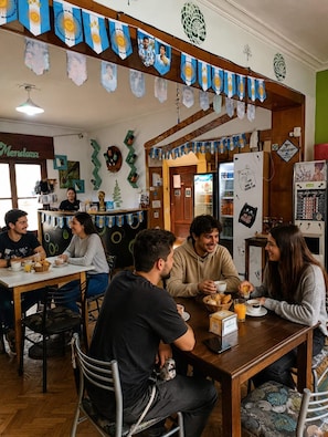 Un café avec des meubles en bois, un réfrigérateur et un mur décoré de drapeaux et d’une fresque.