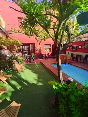 Um pátio com piscina, espreguiçadeiras de madeira e área de refeições com mesas e cadeiras.