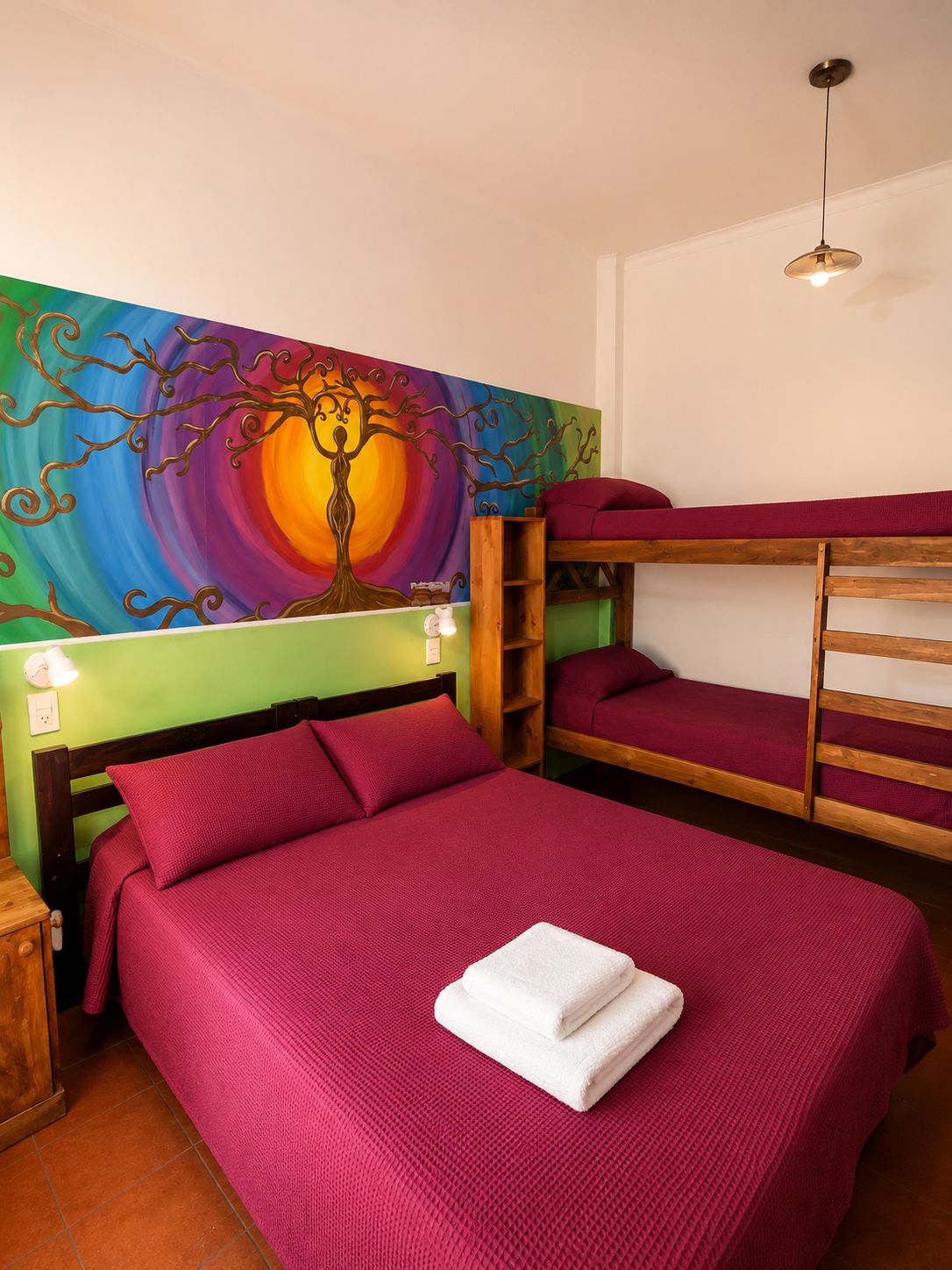 A room with a bunk bed, a colorful mural, a bedside table with a lamp, and a hanging light fixture.