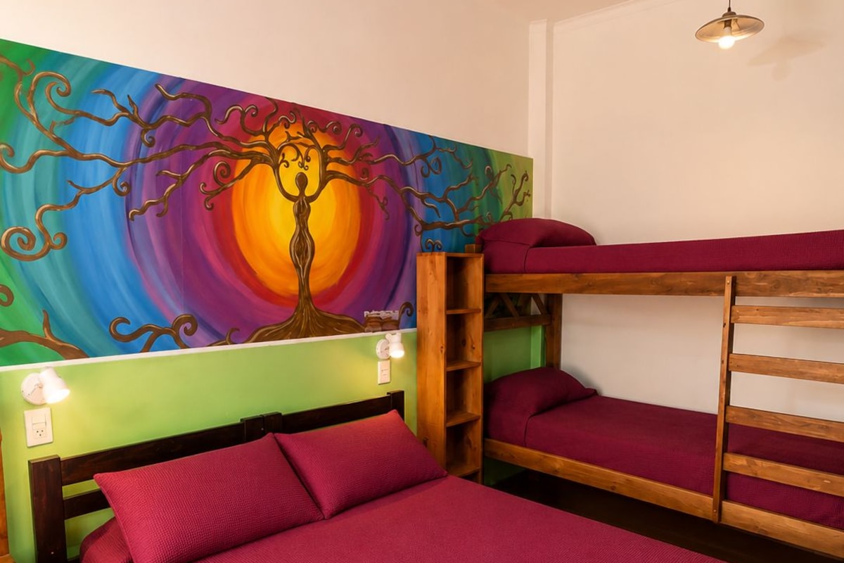 Une chambre avec un lit superposé, une fresque murale colorée, une table de chevet avec une lampe et un luminaire suspendu.