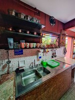 Una cocina con electrodomésticos de acero inoxidable, un lavamanos y una ventana con plantas.